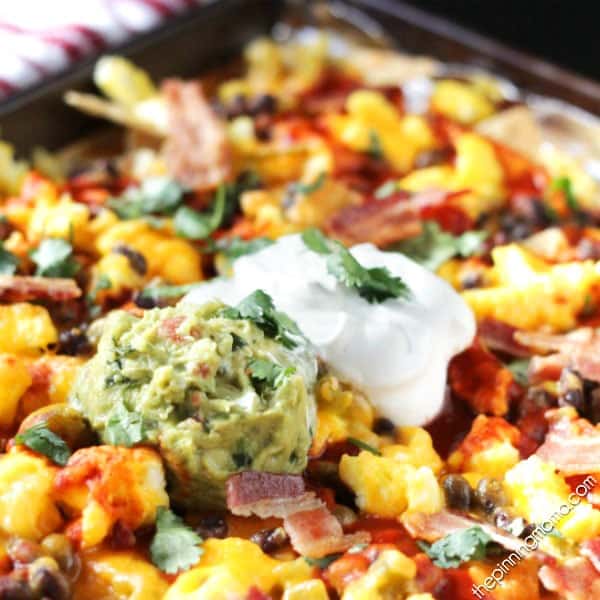 Breakfast Nachos Recipe - This quick and easy breakfast recipe will become a quick favorite if you love nachos as much as we do! Crispy tortilla chips are layered with eggs, bacon, enchilada sauce and a few other ingredients to make a breakfast to feed 2 or feed a crowd in just minutes.